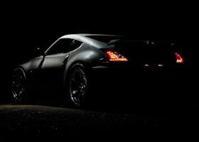 A dramatic shot of a Nissan 370Z sports car illuminated in darkness with vibrant tail lights.